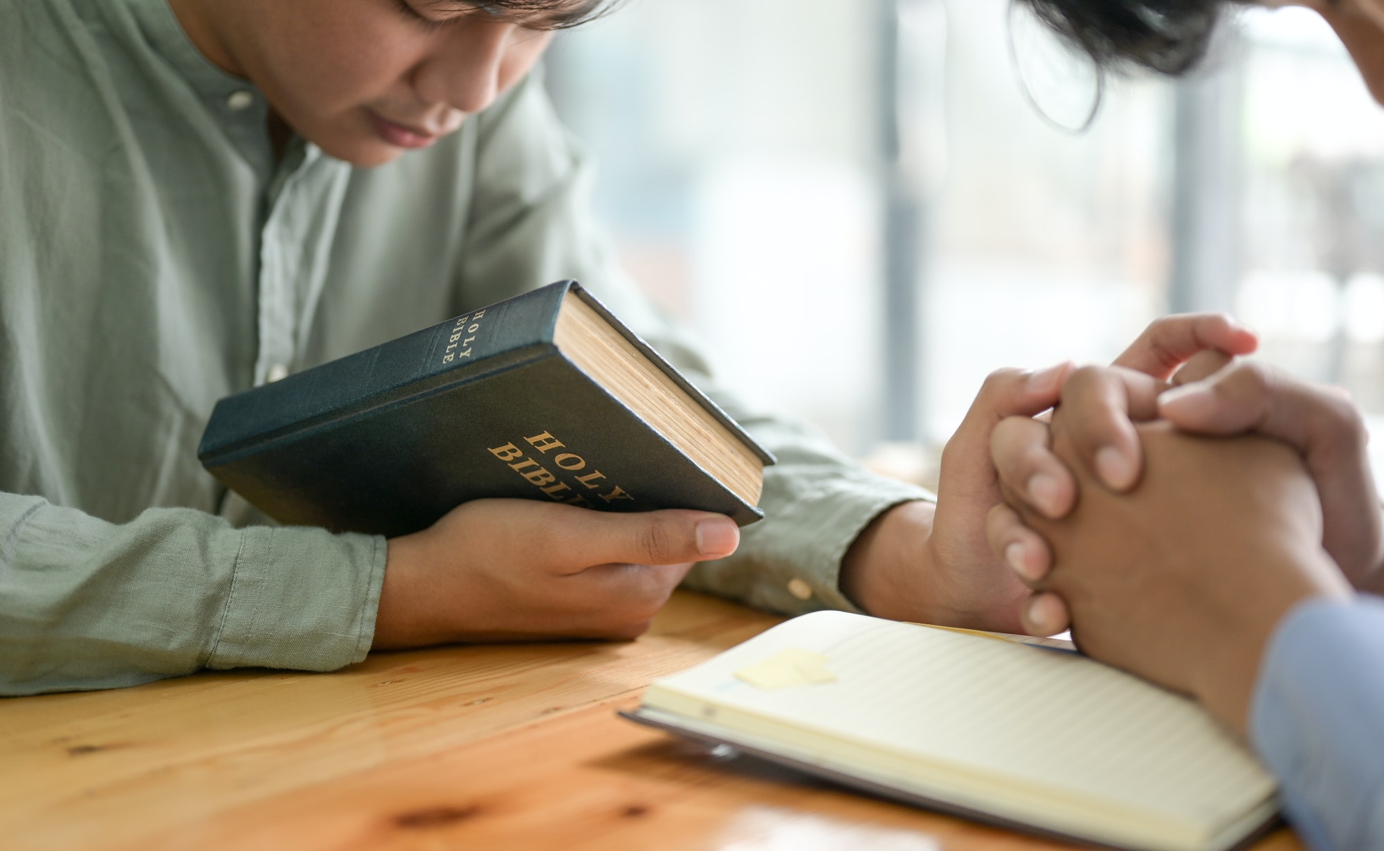 Close-up shot of The Bible and people praying.